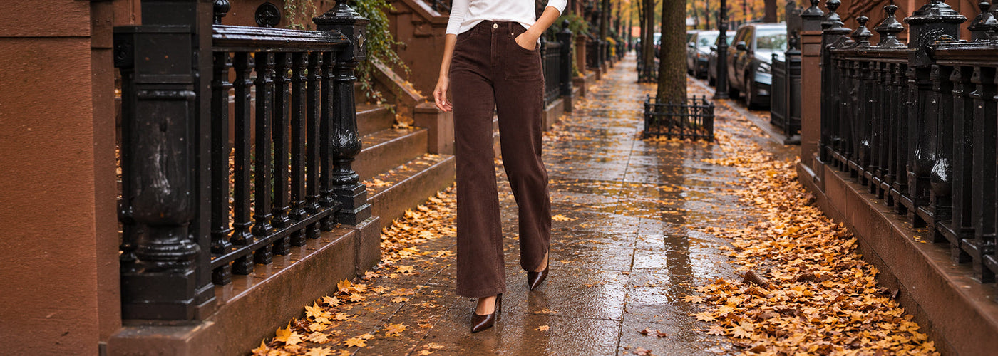 Jeans brun à jambe droite porté avec un haut blanc et des escarpins bruns dans une rue aux couleurs d’automne.