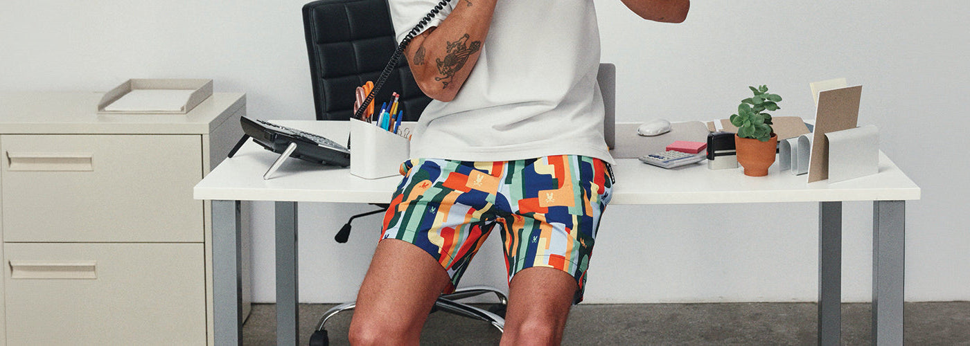 Short maillot multicolore à imprimé graphique porté avec un T-Shirt blanc dans un décor de bureau contemporain.