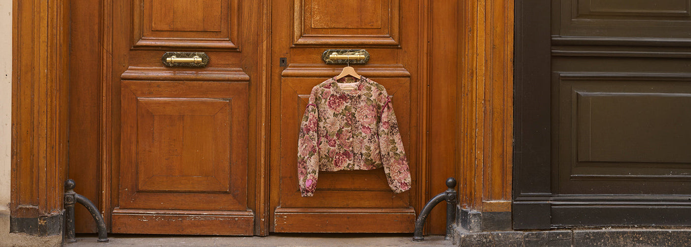 Haut fleuri rose et vert suspendu devant une porte en bois, pièce féminine à imprimé floral pour une garde robe colorée.