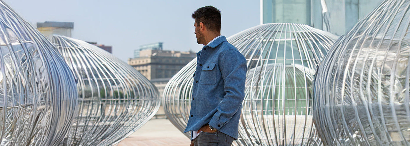 Modèle homme portant une surchemise bleu clair dans un décor architectural moderne. Surchemises Au Noir idéales pour superposer avec style lors des saisons intermédiaires.