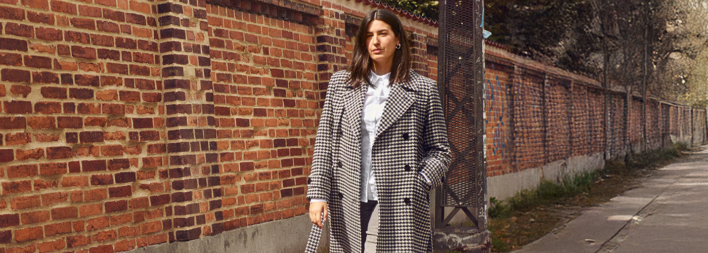 Collection Femme Printemps-Été 2024 : Un mannequin élégant pose dans une robe fleurie vibrante et des talons roses, sur un fond aux tons neutres avec des accessoires artistiques, incarnant l'élégance et la fraîcheur saisonnière