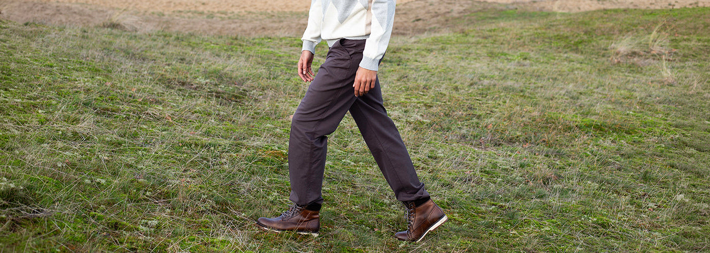 Pantalon brun à coupe décontractée porté avec un tricot à motif losanges et des bottines en cuir, mode homme en extérieur.