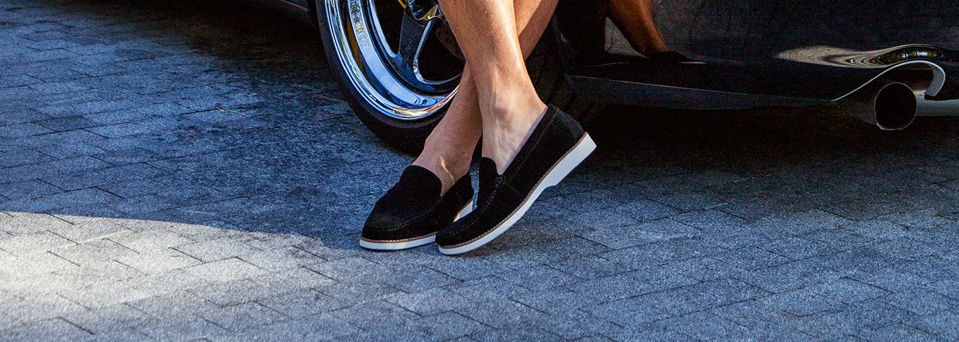 Vue rapprochée de souliers noirs modernes portés avec bermuda devant une voiture sportive. Souliers Au Noir élégants combinant style urbain et confort.