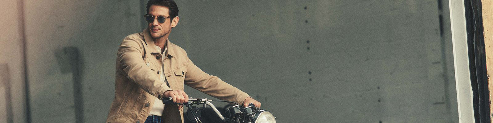 Un homme sur une moto avec un jacket beige uni et des lunettes fumées