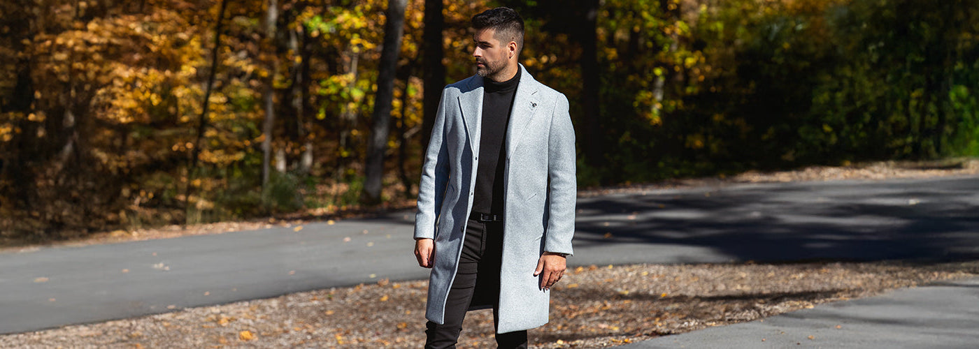 Modèle homme portant un manteau gris élégant marchant sur une route entourée de forêt. Manteaux Au Noir stylés parfaits pour les saisons froides.