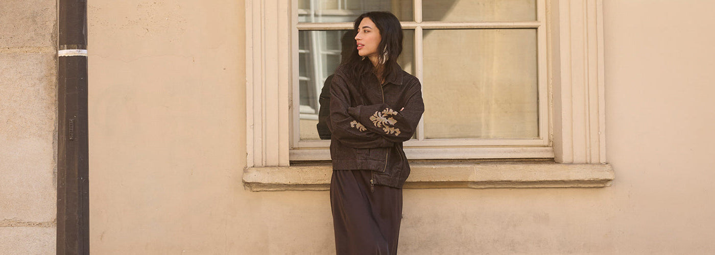 Femme portant une veste brune brodée avec pantalon assorti devant une fenêtre, look féminin de la collection Cream.