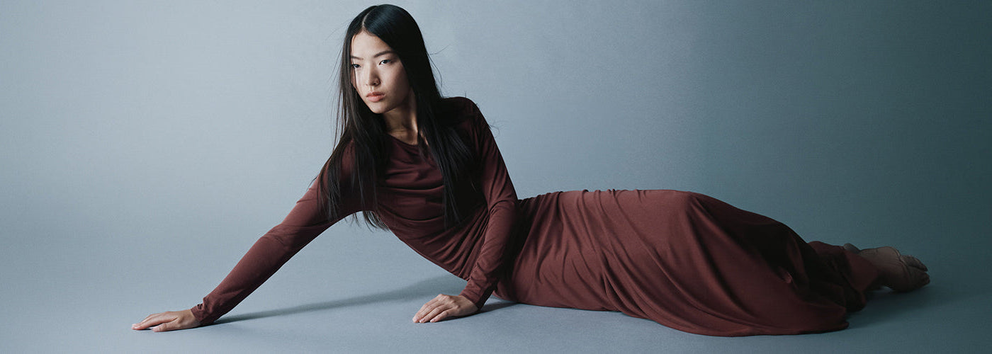 Femme portant une longue robe bordeaux à manches longues dans un décor minimaliste gris, look élégant de la collection HUGO.