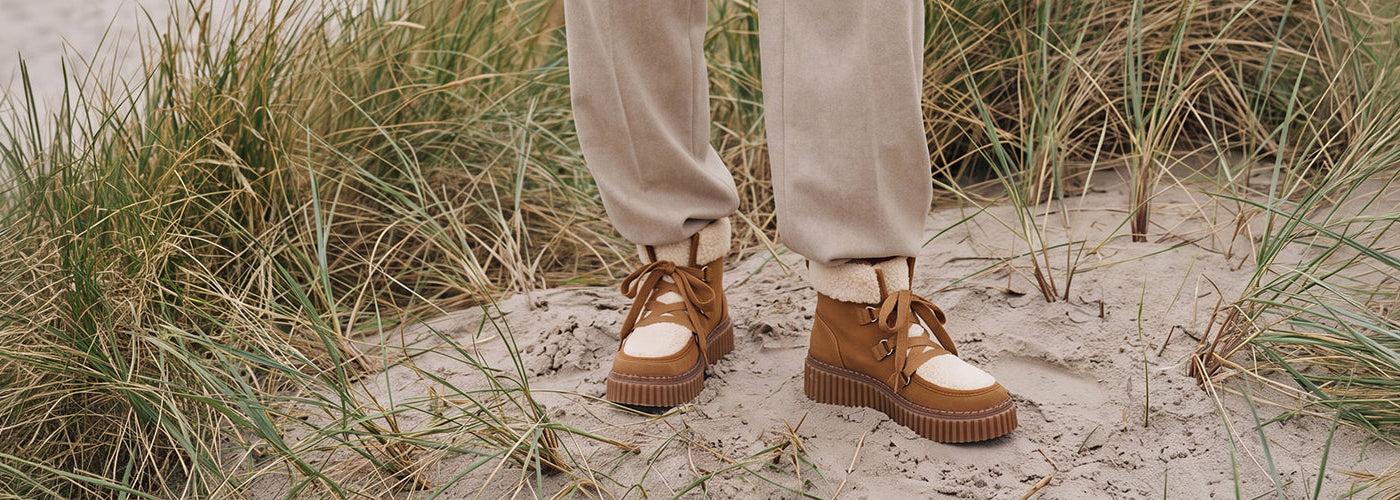 Bottines brunes à lacets avec empiècements crème et semelles crantées, chaussures pour femme présentées dans un décor naturel.
