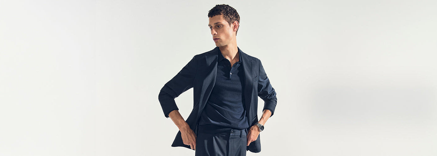 Homme élégant portant un ensemble bleu marine composé d’un Veston ajusté et d’un pantalon habillé, accompagné d’un polo ton sur ton.