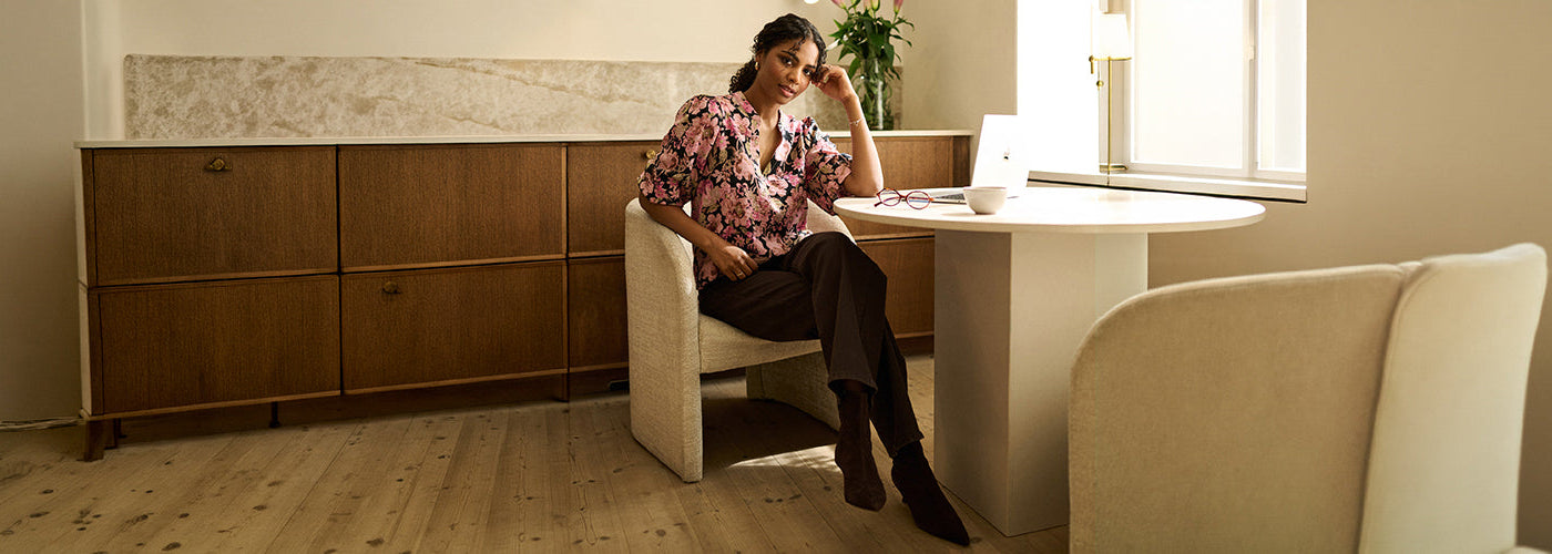 Femme portant une blouse florale rose et noire avec pantalon foncé, look féminin de la collection Kaffe.