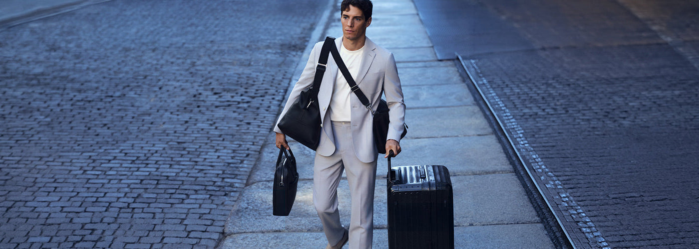 Ensemble habillé beige accompagné de sacs noirs et d’une valise, sélection d’accessoires pour homme au style urbain.