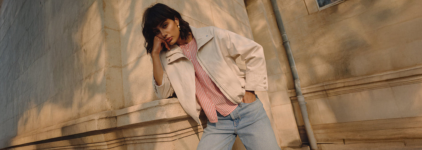 Silhouette féminine moderne portant une veste claire et un jean bleu dans un décor urbain lumineux inspiré du style européen contemporain et décontracté.