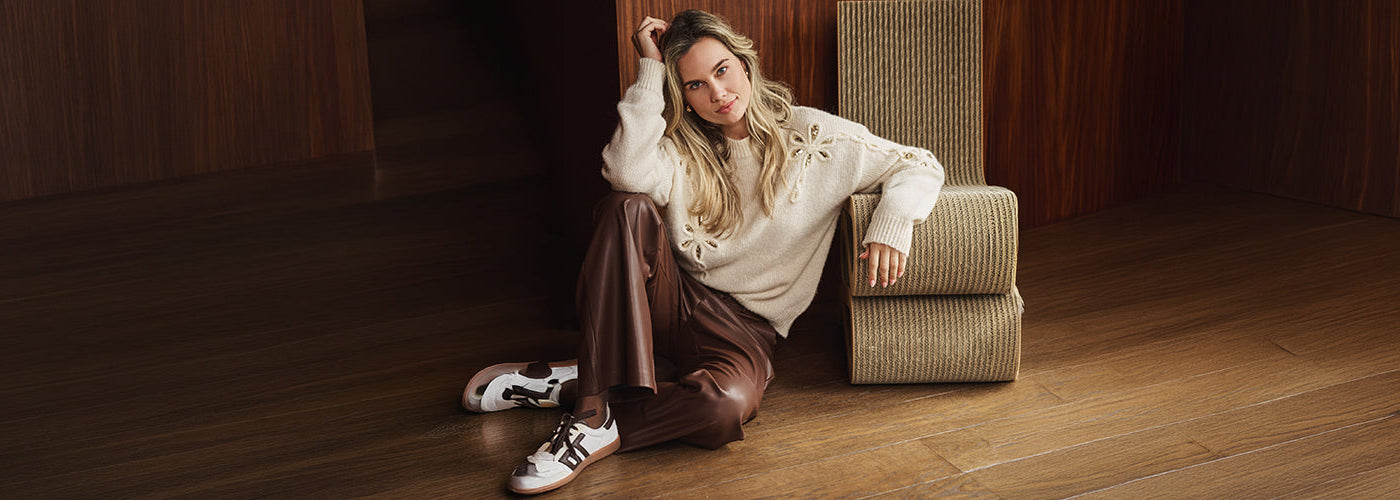 Femme portant un tricot crème ajouré avec pantalon brun effet cuir, look automne de la collection EsQualo.
