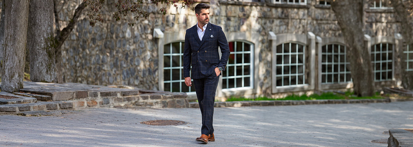 Modèle homme élégant portant un complet beige devant une résidence luxueuse entourée de jardins modernes. Habits Au Noir sophistiqués pour un style distingué et contemporain.