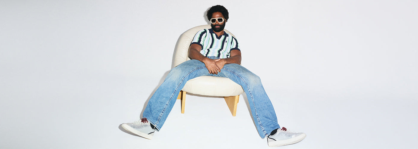 Homme portant un polo rayé vert, blanc et marine avec jeans, look décontracté de la collection Psycho Bunny.
