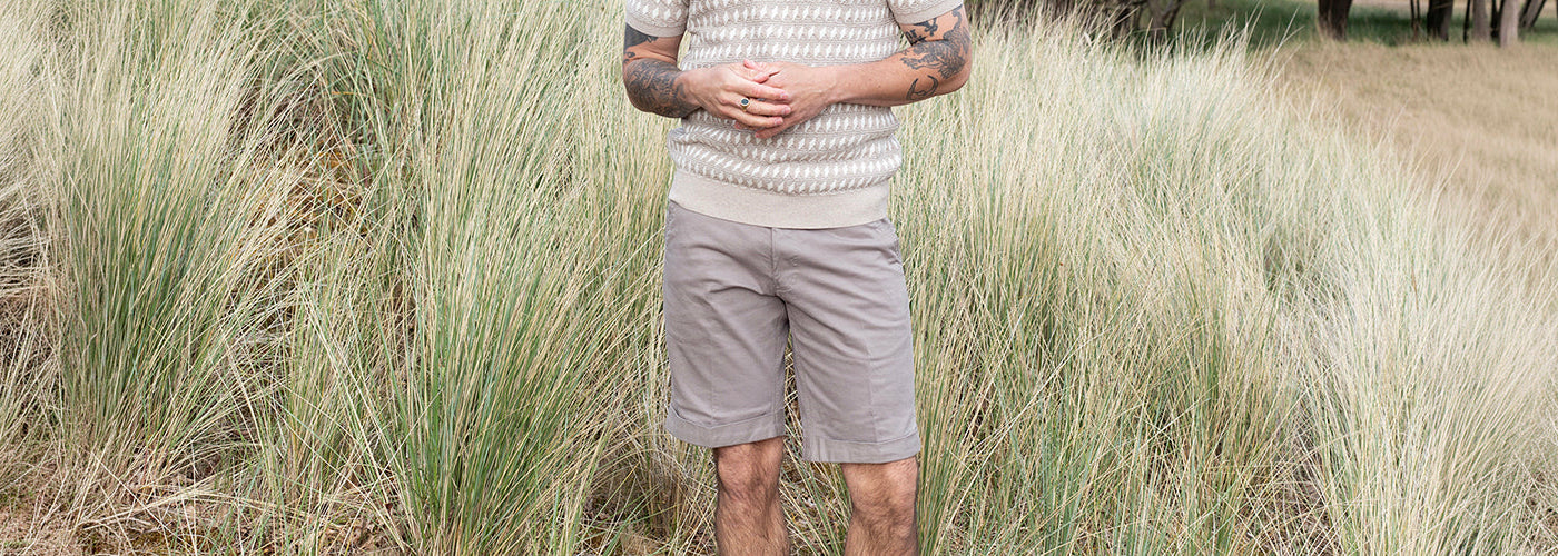 Short beige porté avec un tricot M.C. texturé dans un paysage de hautes herbes, tenue estivale décontractée pour homme.