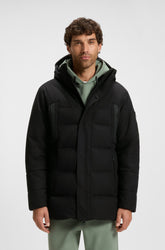 Vue avant sur modèle du manteau d’hiver noir à capuchon avec rabat et poches zippées pour homme par HUGO BOSS