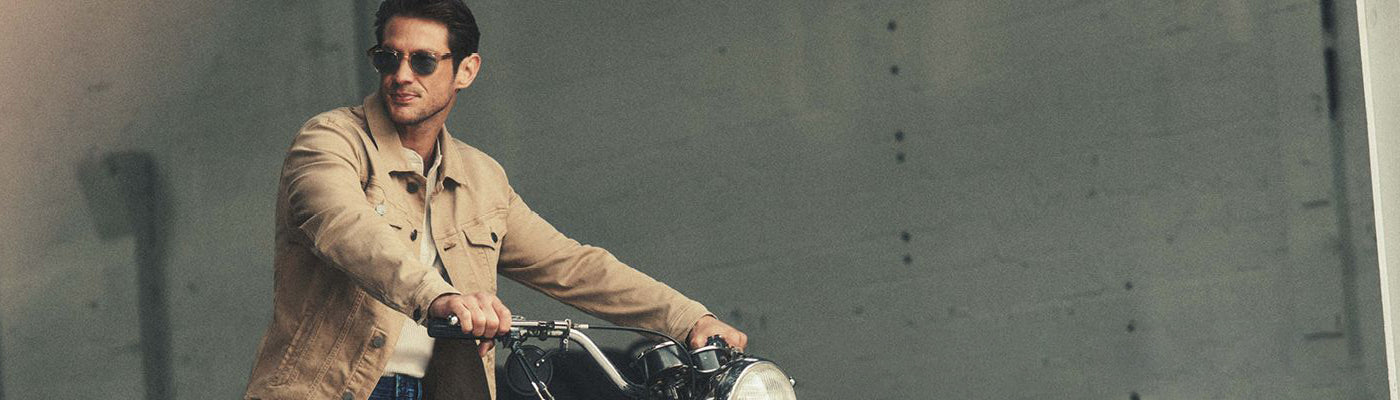Un homme sur une moto avec un jacket beige uni et des lunettes fumées