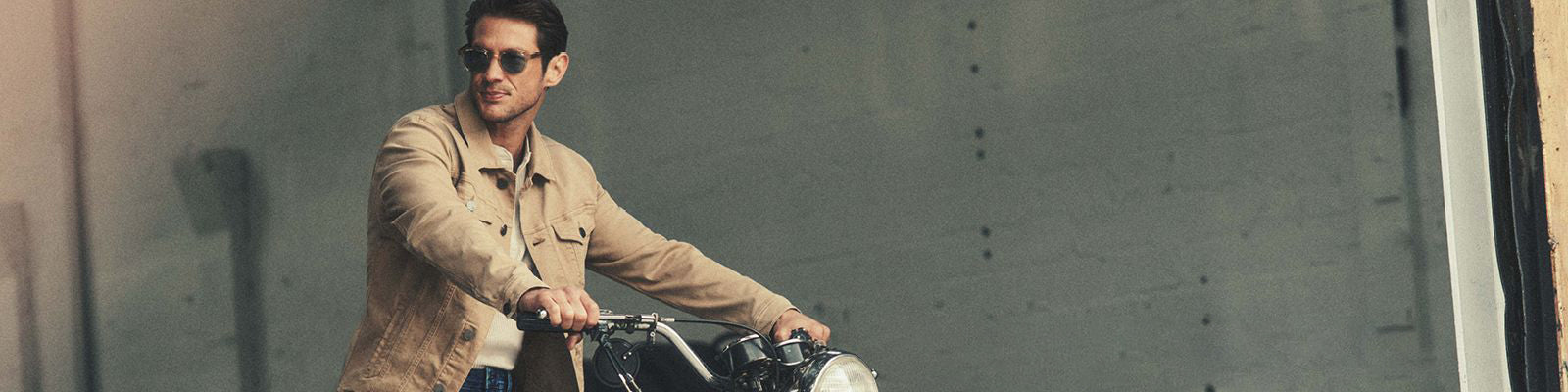 Un homme sur une moto avec un jacket beige uni et des lunettes fumées