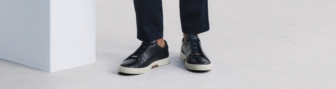 Chaussures sport noires en cuir avec semelles contrastantes, portées avec un pantalon marine court à la cheville.