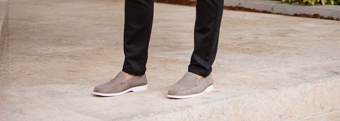 Gros plan sur les pieds d’un modèle homme portant souliers beige avec pantalon noir sur des marches en pierre. Collection souliers hommes élégants et chaussures habillées.