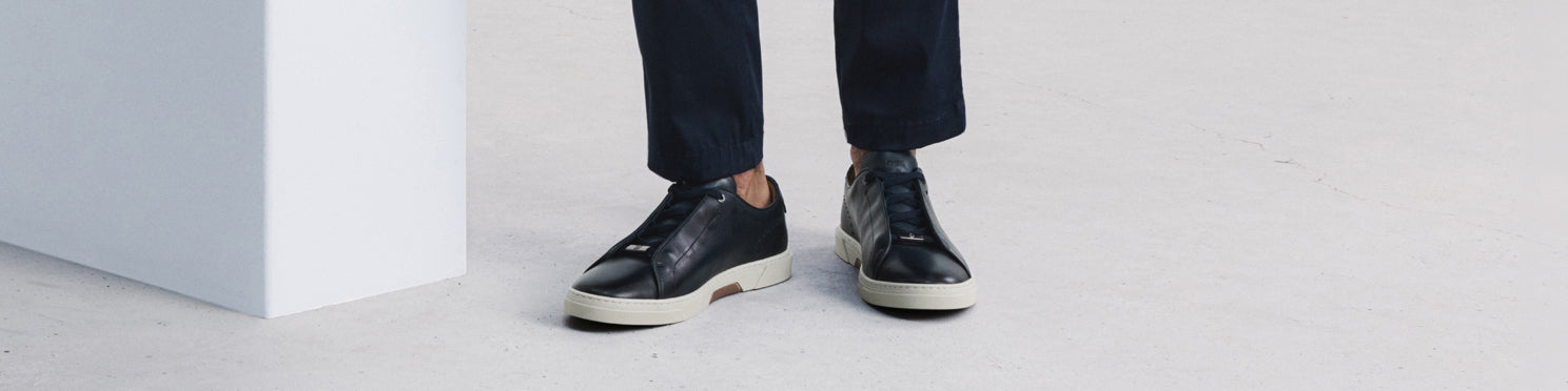 Black leather sneakers with contrasting soles, styled with navy ankle length pants.