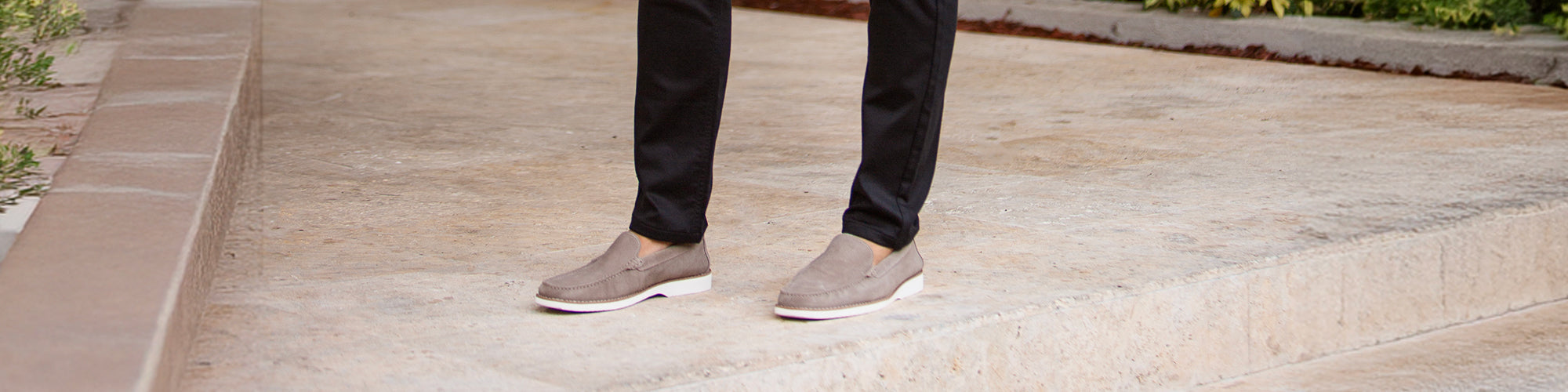 Gros plan sur les pieds d’un modèle homme portant souliers beige avec pantalon noir sur des marches en pierre. Collection souliers hommes élégants et chaussures habillées.