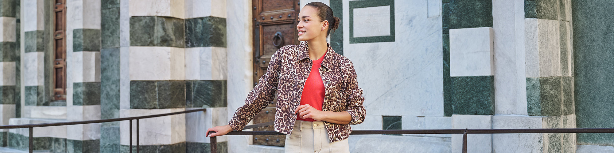 Modèle femme portant une veste imprimée léopard avec haut rouge devant une architecture classique en pierre. Collection vestes femmes mode et vestes tendance.