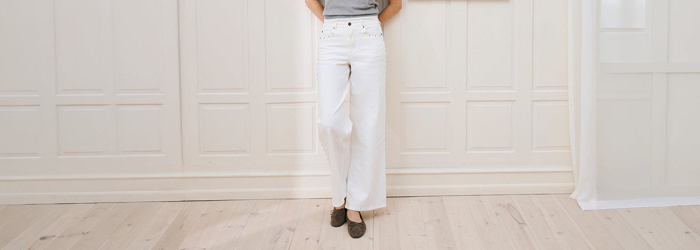 Modèle femme portant pantalon blanc et chaussures plates dans un intérieur lumineux minimaliste avec plancher de bois. Collection pantalons femmes élégants et pantalons confortables.