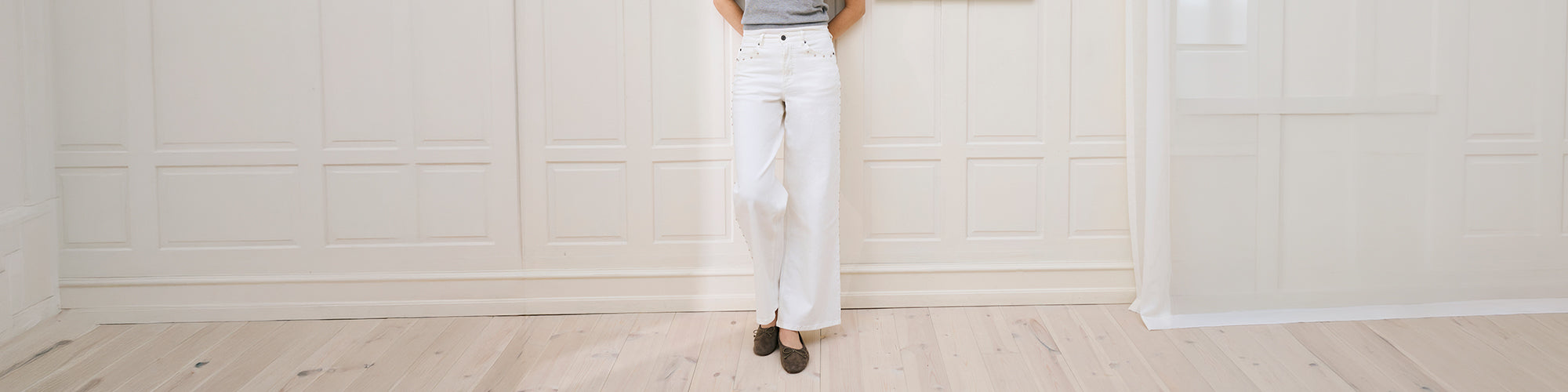 Modèle femme portant pantalon blanc et chaussures plates dans un intérieur lumineux minimaliste avec plancher de bois. Collection pantalons femmes élégants et pantalons confortables.