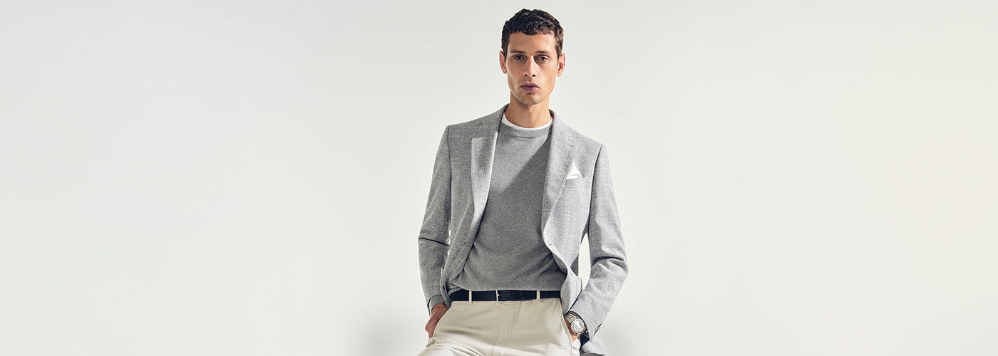 Modèle homme portant un veston gris avec pantalon beige dans un décor studio épuré. Collection vestons hommes élégants et vestons habillés.