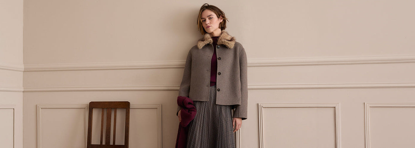 Femme portant une veste courte taupe à col en fausse fourrure, jupe midi à carreaux et accessoires bordeaux, look automne OUI pour femme.