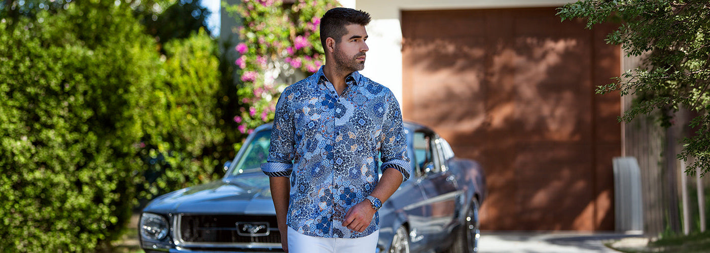 Modèle homme portant une chemise bleue à motifs devant une voiture classique dans un jardin ensoleillé. Collection chemises hommes élégantes et chemises habillées tendance.
