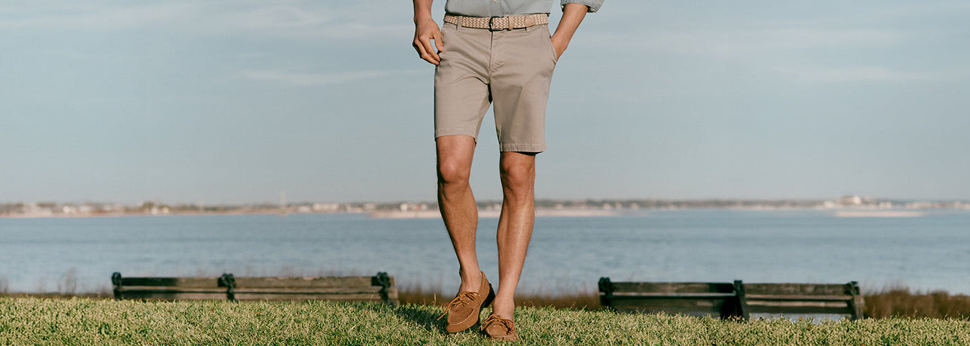 Modèle homme marchant près de l’eau portant shorts beige et mocassins dans un paysage côtier. Collection shorts hommes élégants et shorts d’été.