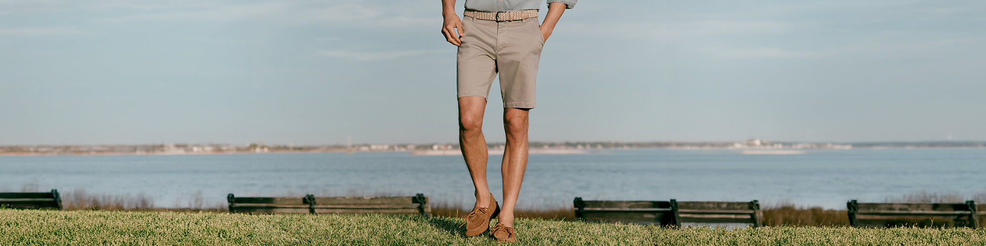 Modèle homme marchant près de l’eau portant shorts beige et mocassins dans un paysage côtier. Collection shorts hommes élégants et shorts d’été.