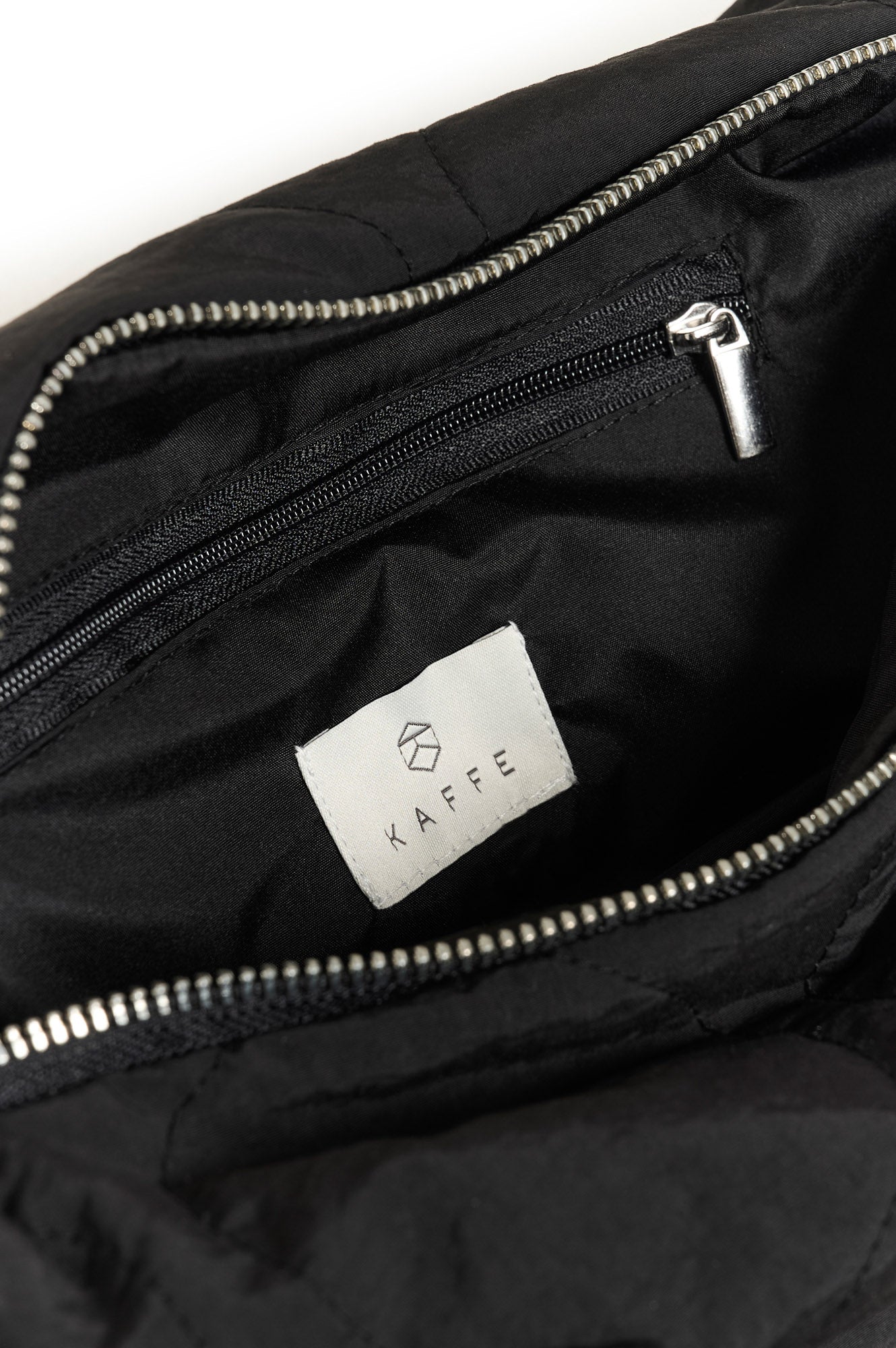 Détail intérieur de la sac à bandoulière noir avec poche zippée ainsi que dents métalliques et étiquette KAFFE pour femme