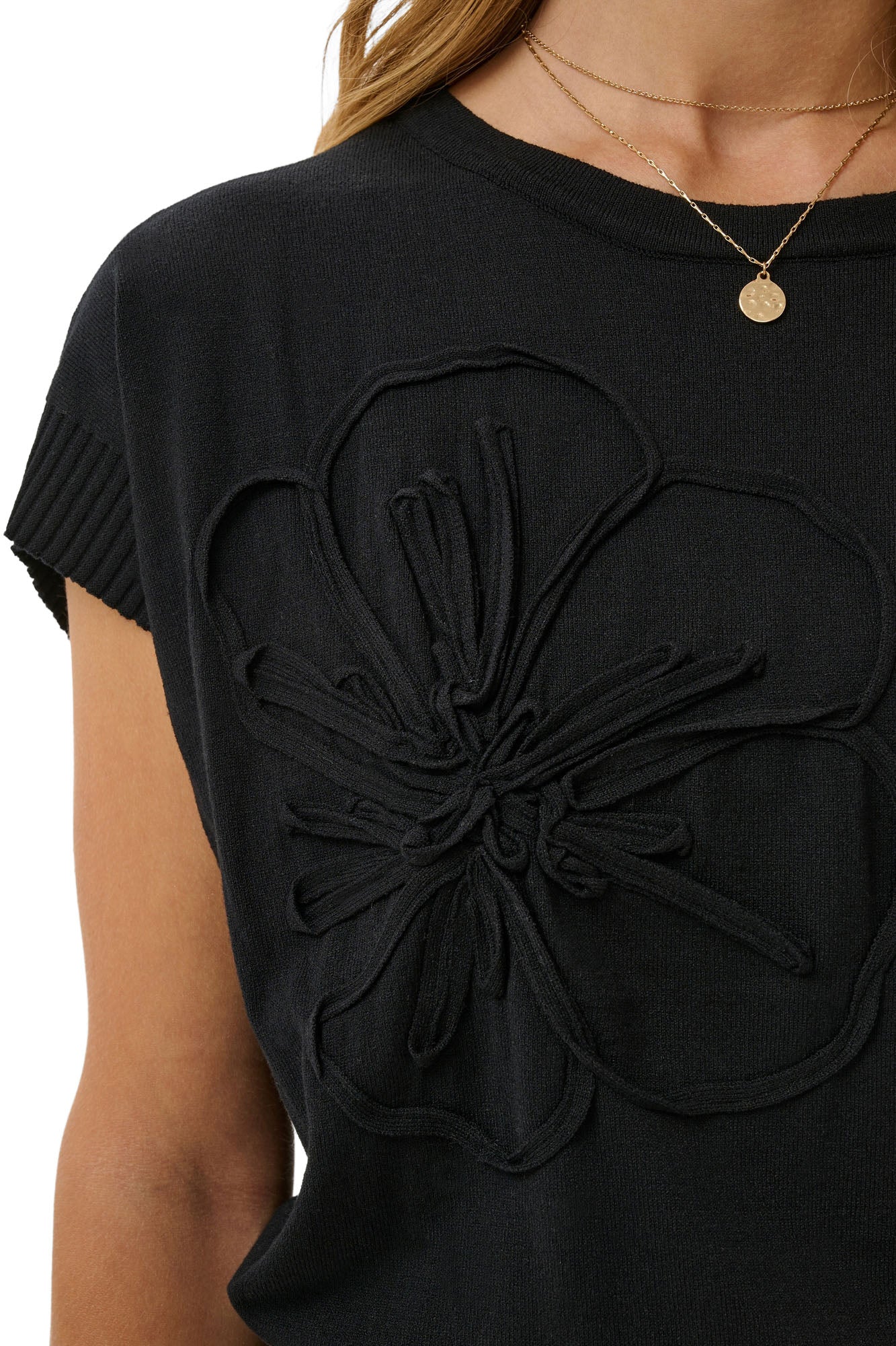 Cream women's black knit Short-sleeve T-Shirt showing ribbed crew neck, sleeve cuff, and raised floral appliqué, close-up