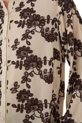 Women's close detail of dark brown floral embroidery and button placket on cream long-sleeve blouse fabric