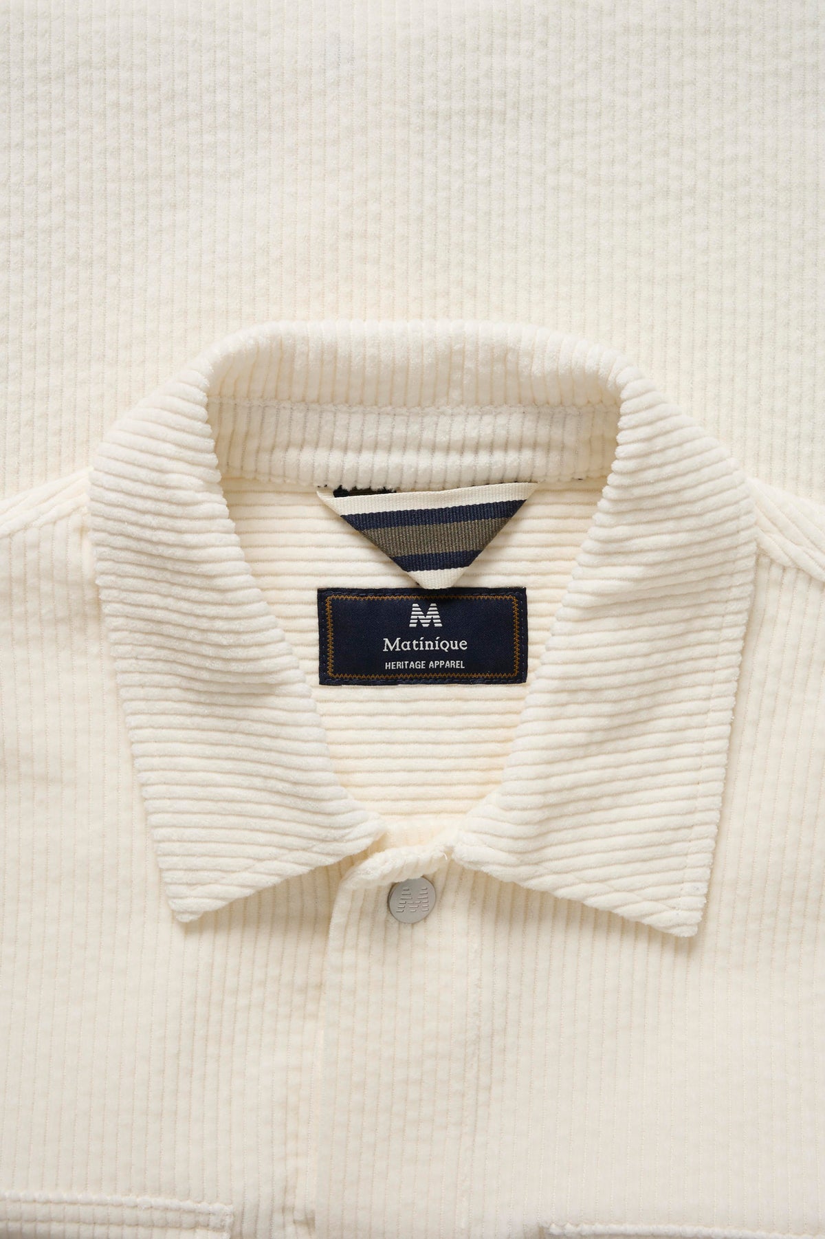 Détail du col de chemise à manches longues en velours côtelé ivoire avec étiquette et ganse rayée pour homme par Matinique