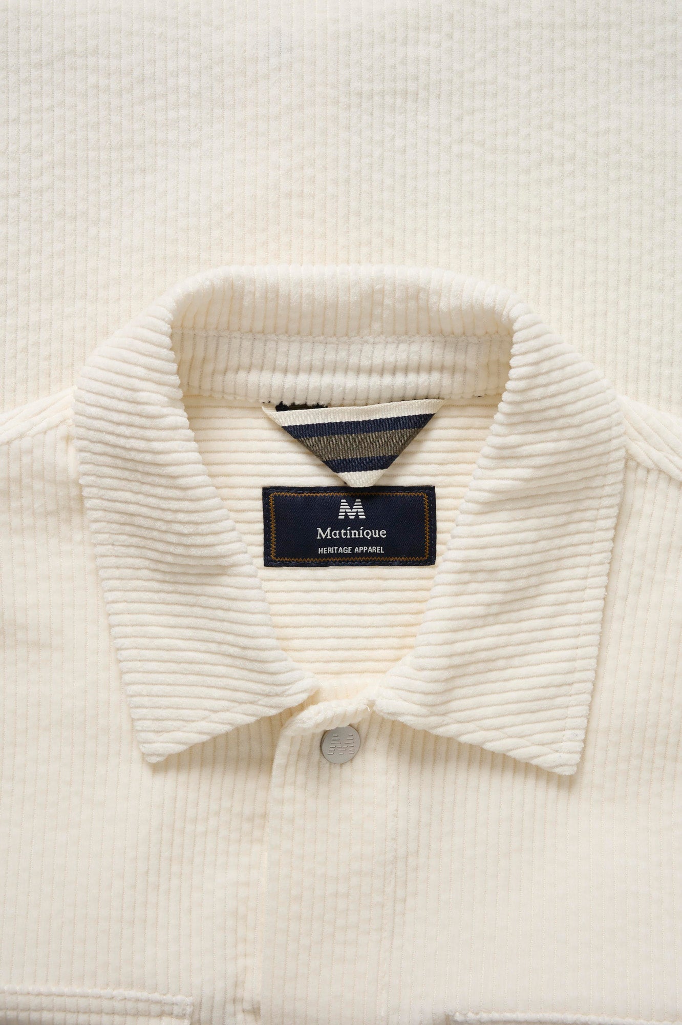 Détail du col de chemise à manches longues en velours côtelé ivoire avec étiquette et ganse rayée pour homme par Matinique