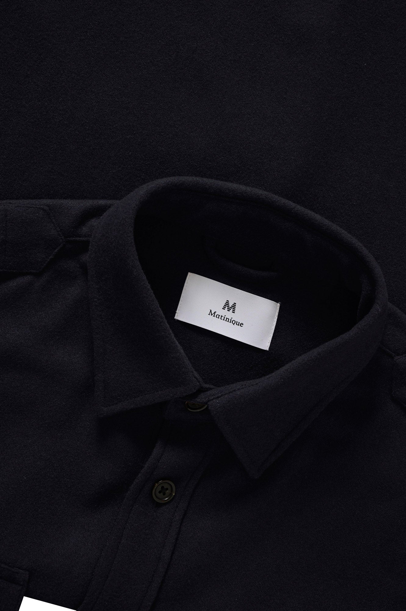 Close-up of men's black overshirt collar, button placket, brushed texture, and inner label by Matinique