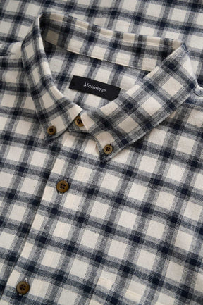 Matinique men's close detail of ivory and navy plaid long-sleeve shirt collar, tan buttons, and woven texture