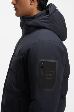 Men's side close-up of dark navy padded winter jacket with hood and BOSS sleeve zip patch by HUGO BOSS