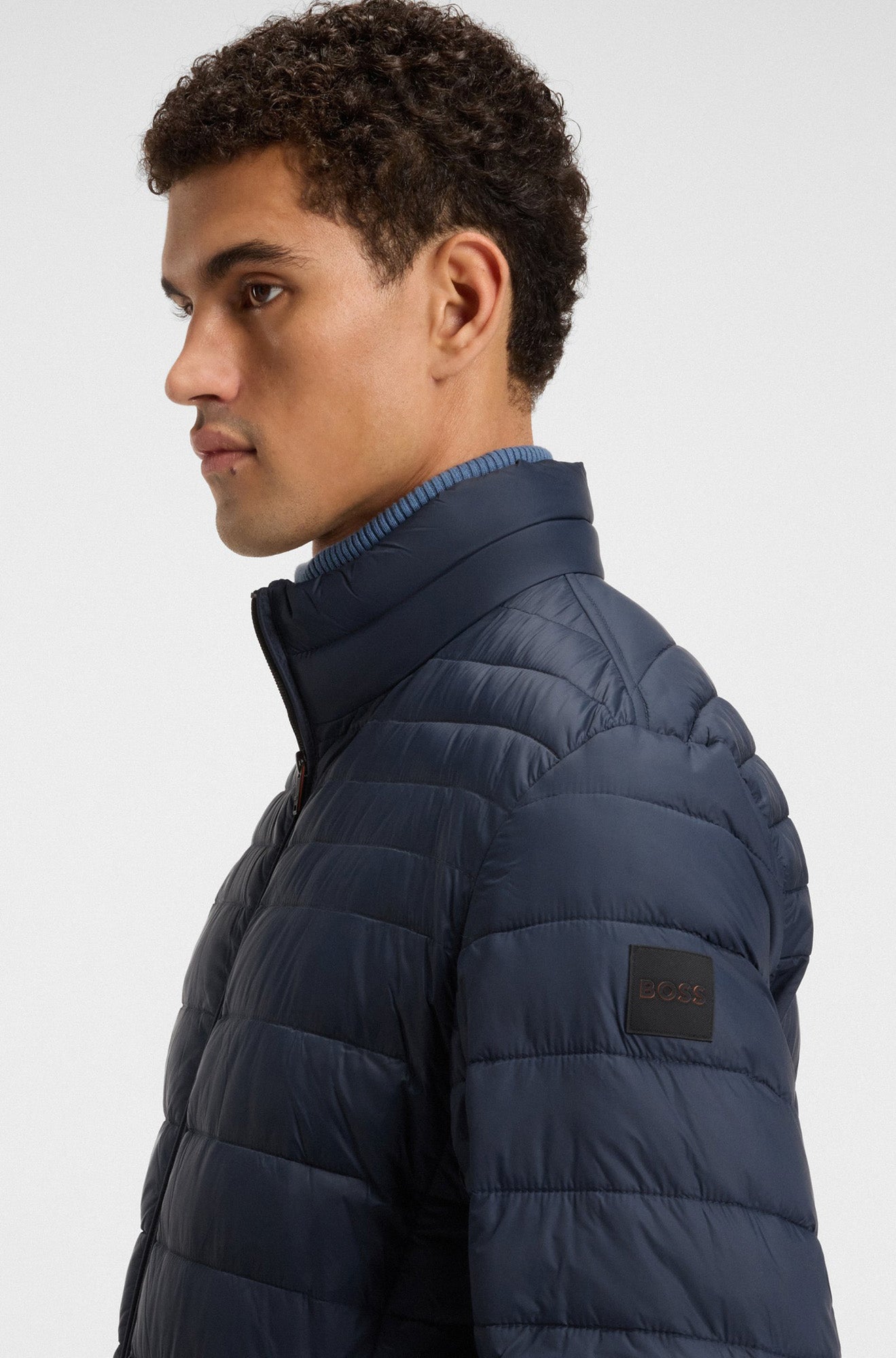 Manteau d'hiver matelassé marine avec col montant et écusson BOSS noir à la manche pour homme par HUGO BOSS, vue de côté