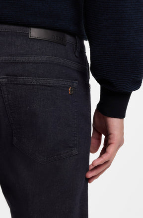 Men's close back model view of dark black straight-leg jeans with BOSS waist patch and logo on back pocket by HUGO BOSS