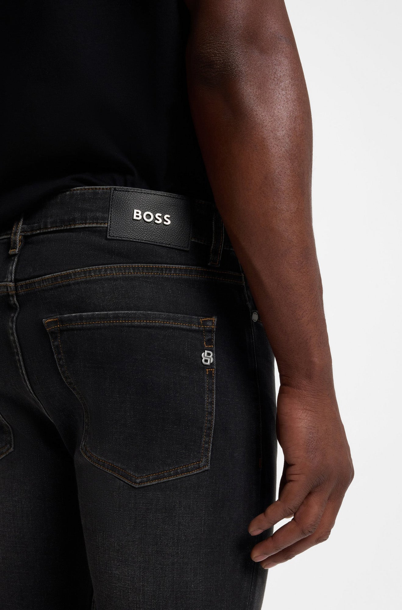 Men's back waist close-up of black straight-leg jeans showing BOSS logo patch and stitched back pocket by HUGO BOSS