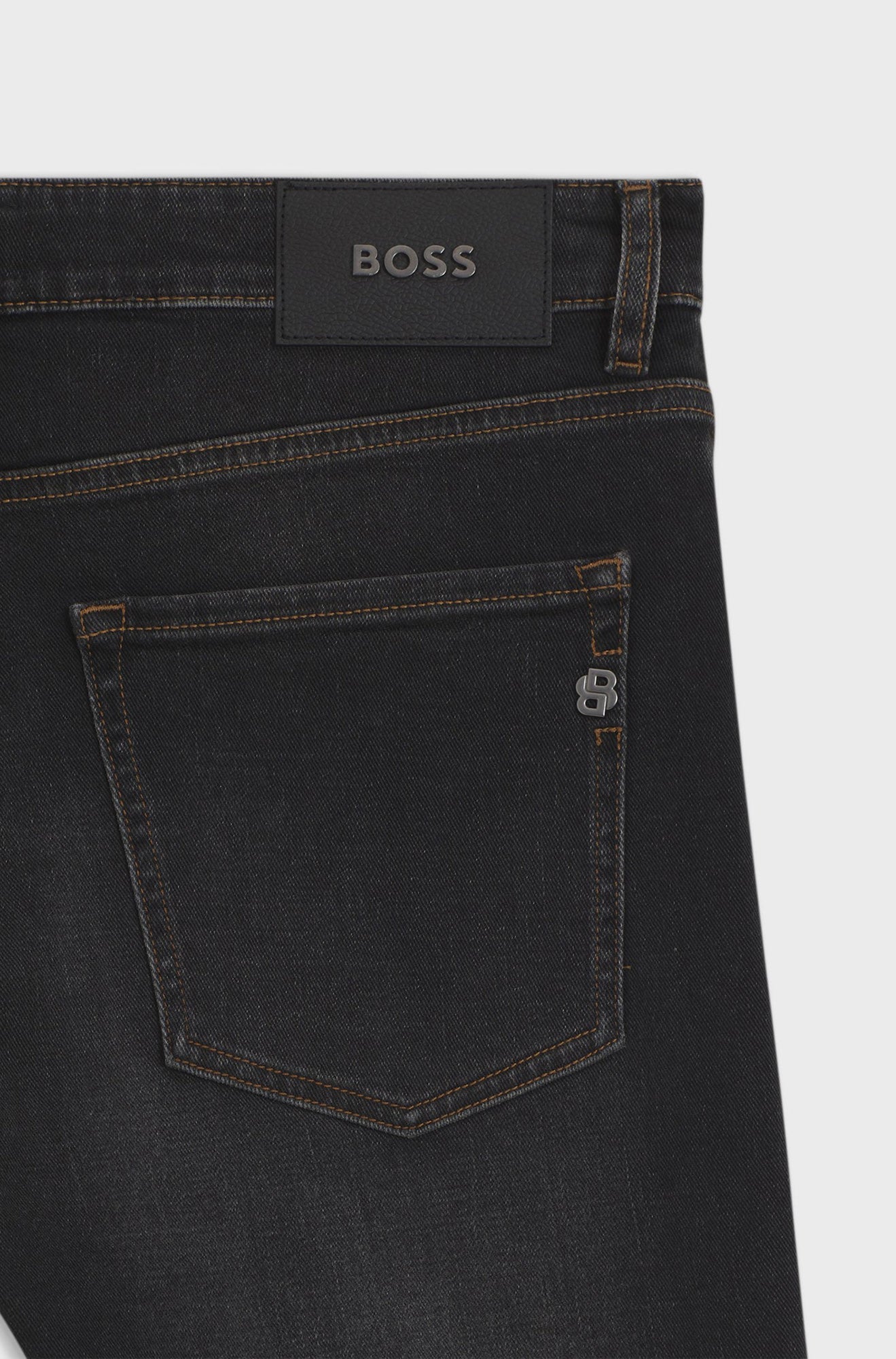 HUGO BOSS men's black straight-leg jeans back pocket with brown stitching, BOSS patch, and metal B trim, close-up