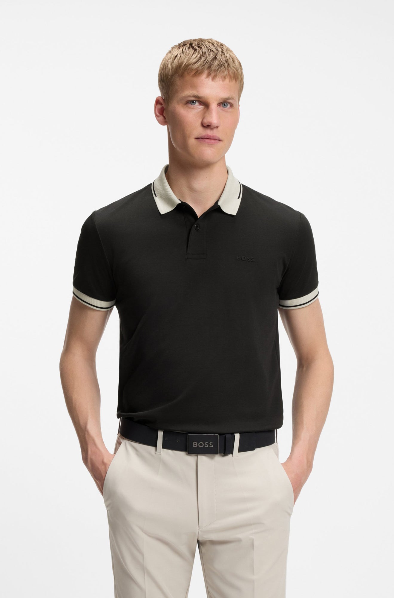 Polo noir porté de face avec col ivoire, poignets rayés et logo ton sur ton pour homme par HUGO BOSS