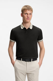 Polo noir porté de face avec col ivoire, poignets rayés et logo ton sur ton pour homme par HUGO BOSS
