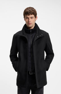 Vue de face d’un manteau d’hiver noir avec col montant, boutons-pression et panneau matelassé pour homme par HUGO BOSS